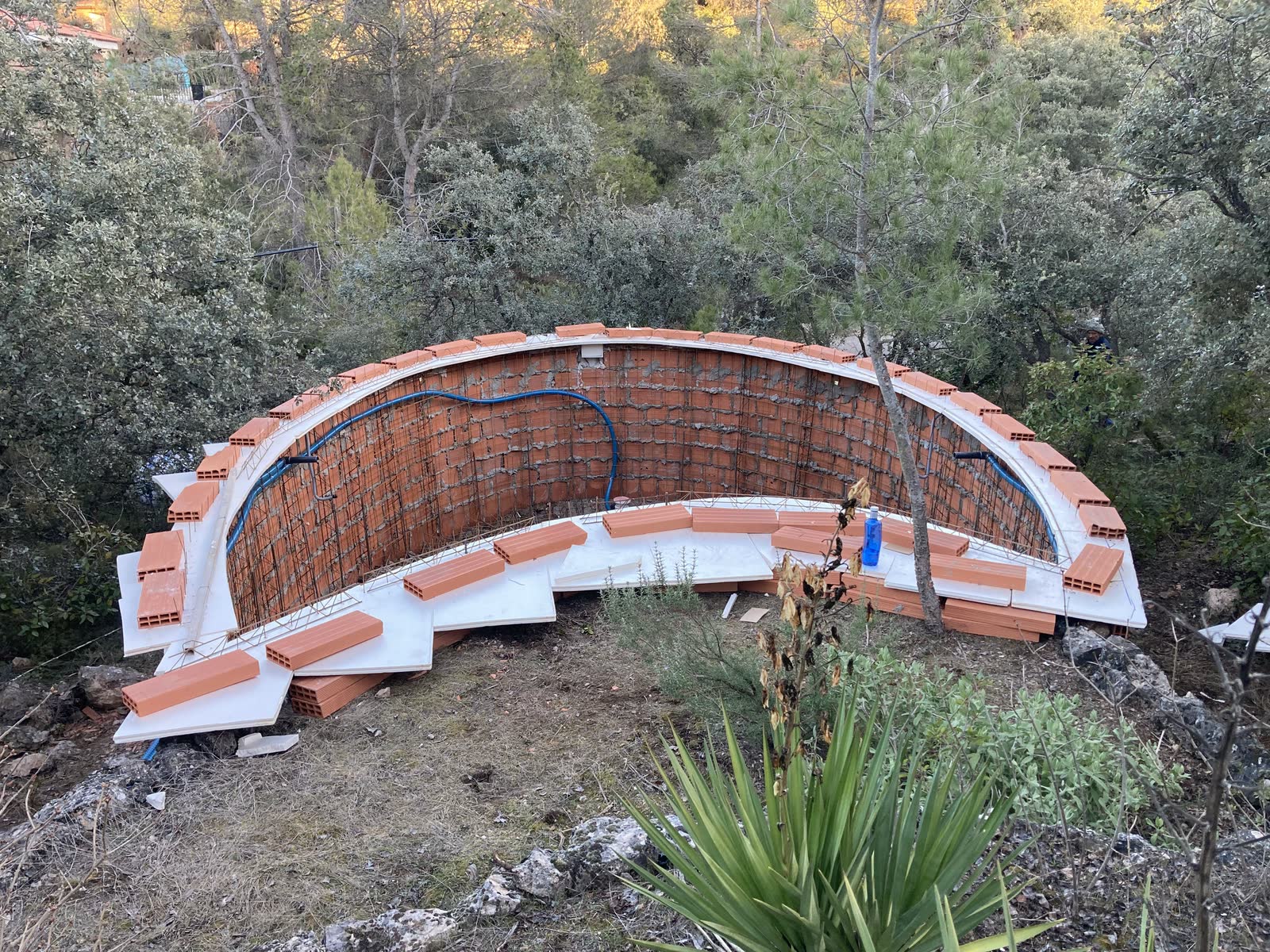 Muro curvo encofrado a una sola cara sobre una ladera, con la armadura vista antes de proyectar el hormigón.