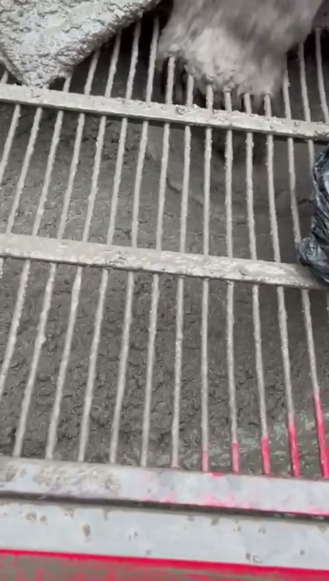 Reja de la tolva de la bomba con el hormigón cayendo dentro, en obra, con el borde rojo de la máquina abajo.